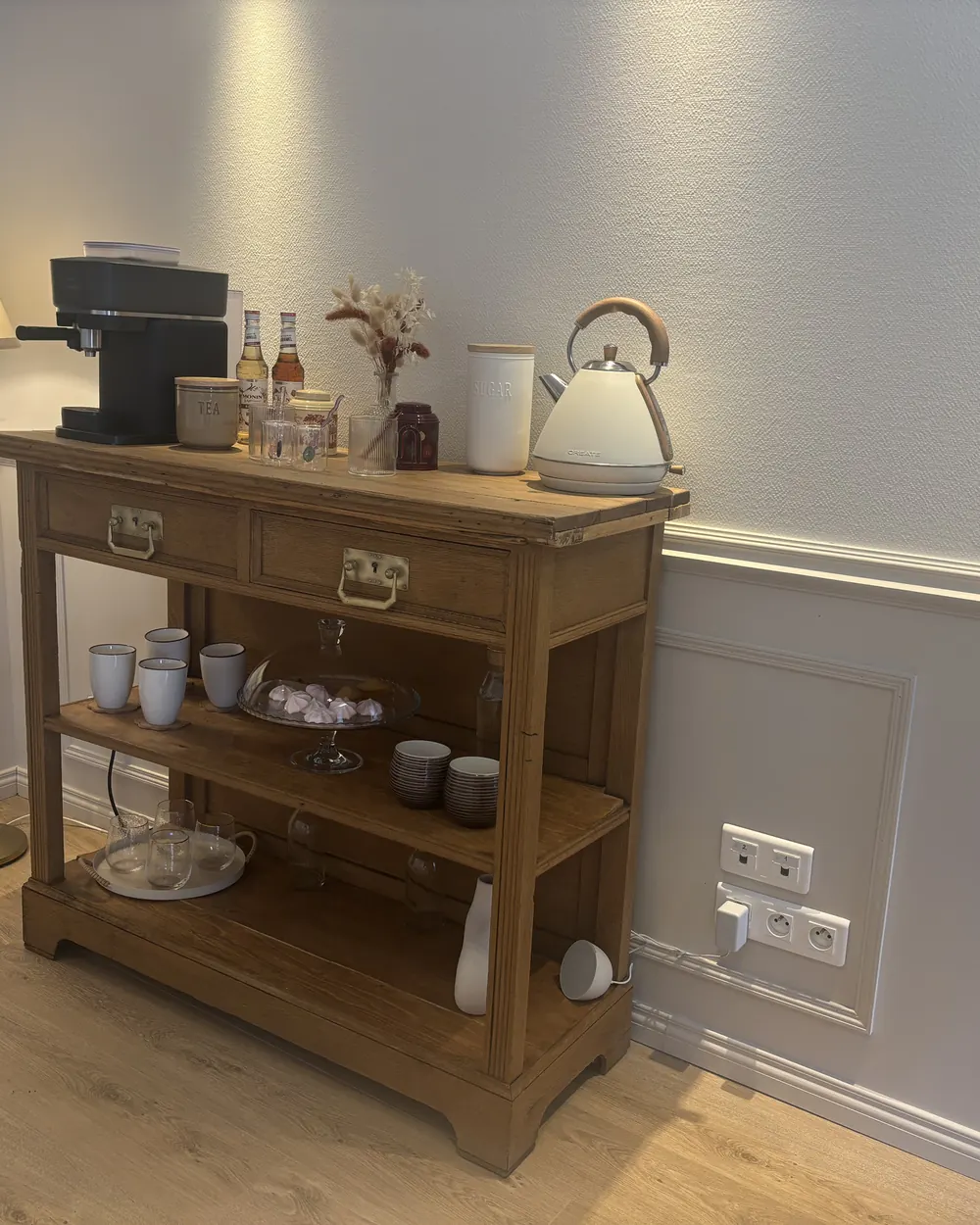 La console à café en bois ancien, avec ses tasses rangées sur l’étagère basse