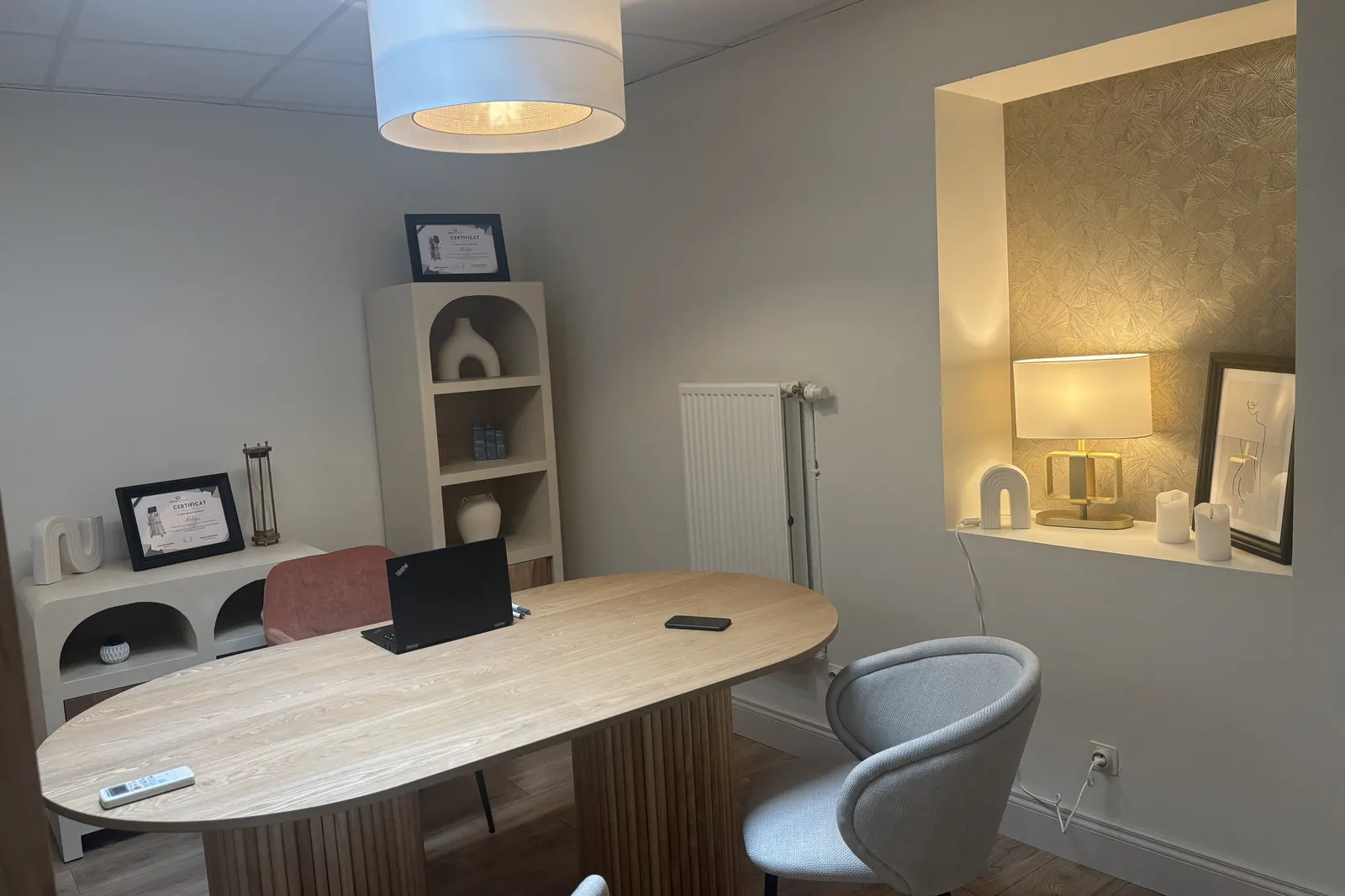 La salle de consultation : table ovale en bois, deux fauteuils, niche éclairée